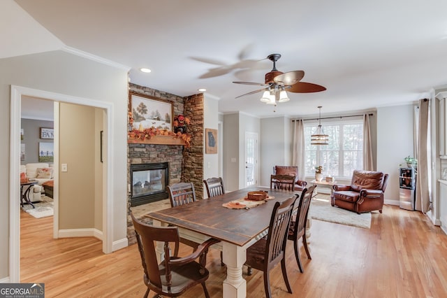 dining area featuring a stone fireplace, light wood-type flooring, baseboards, and ornamental molding