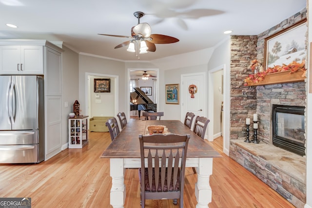 dining area featuring a stone fireplace, light wood-type flooring, baseboards, and ornamental molding