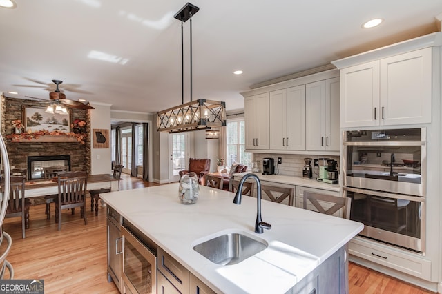 kitchen featuring light wood finished floors, decorative light fixtures, a stone fireplace, appliances with stainless steel finishes, and a sink