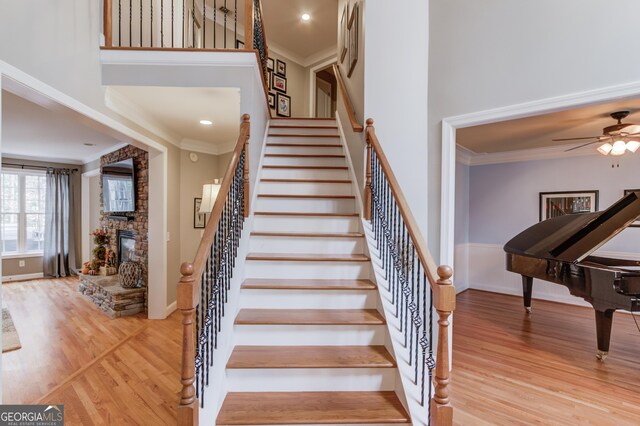 stairway featuring a towering ceiling, a stone fireplace, wood finished floors, and crown molding