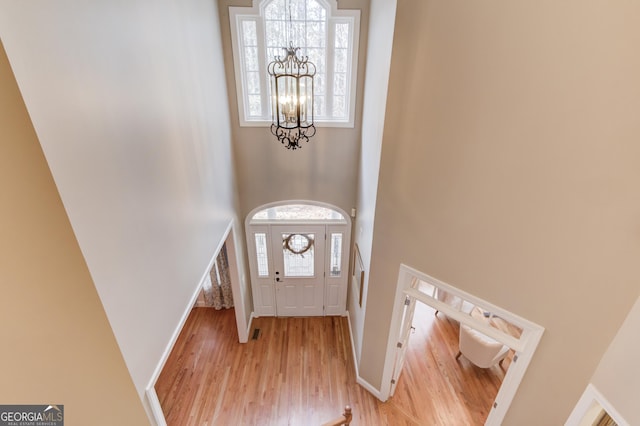 foyer entrance with an inviting chandelier, light wood-style floors, baseboards, and a towering ceiling