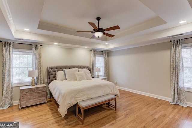 bedroom featuring visible vents, light wood-style flooring, baseboards, and a tray ceiling