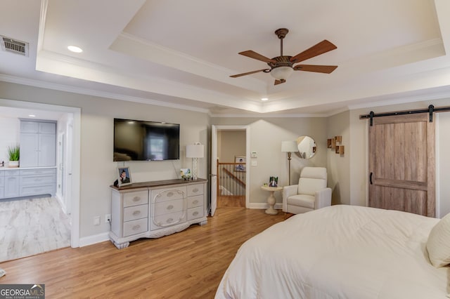 bedroom featuring a barn door, visible vents, light wood-style floors, and a tray ceiling