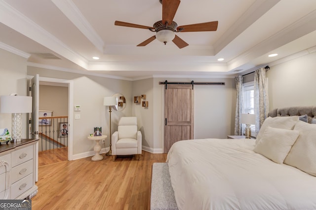 bedroom featuring a barn door, baseboards, light wood-style floors, crown molding, and a raised ceiling