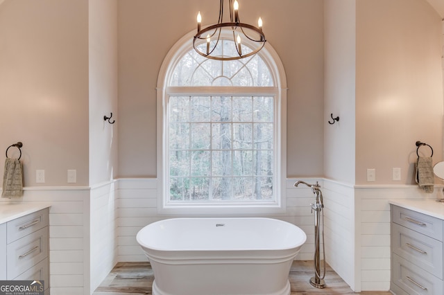 full bath featuring vanity, a soaking tub, a notable chandelier, and a wainscoted wall