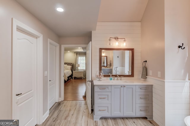 ensuite bathroom featuring connected bathroom, wooden walls, wood finished floors, and vanity