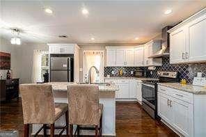 kitchen featuring electric stove, a sink, white cabinetry, freestanding refrigerator, and wall chimney exhaust hood