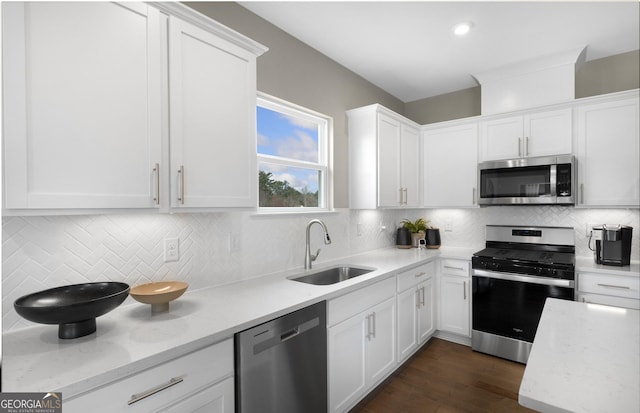 kitchen featuring stainless steel appliances, dark wood-type flooring, a sink, white cabinets, and tasteful backsplash