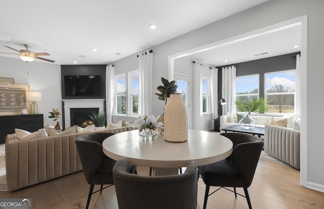 dining space featuring light wood-style floors, a warm lit fireplace, visible vents, and plenty of natural light