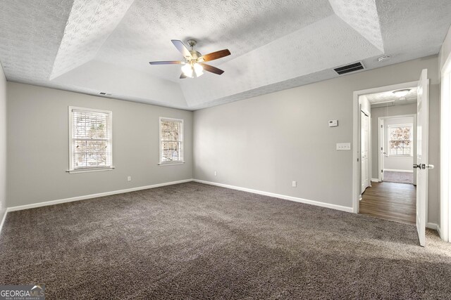 carpeted spare room featuring a ceiling fan, a tray ceiling, a textured ceiling, and baseboards