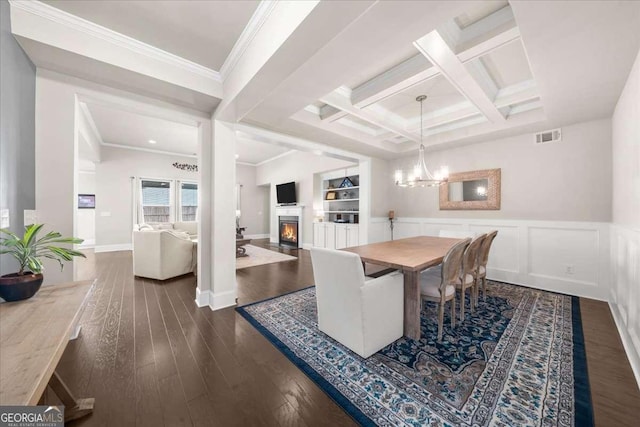 dining area featuring dark wood finished floors, visible vents, ornamental molding, coffered ceiling, and a lit fireplace