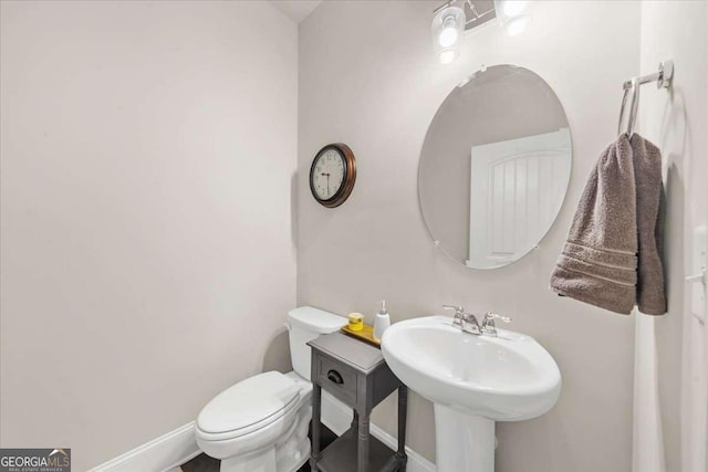 half bath with toilet, baseboards, and a sink