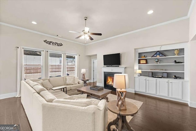 living area with dark wood-style floors, crown molding, a glass covered fireplace, ceiling fan, and baseboards