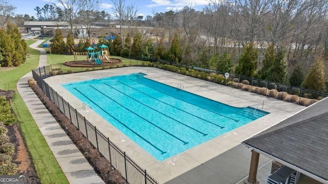 community pool with a lawn, fence, playground community, and a patio