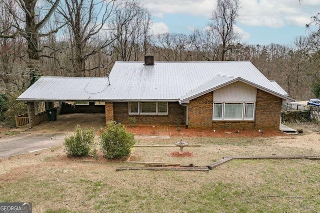 view of front of home with driveway, a chimney, metal roof, an attached carport, and brick siding