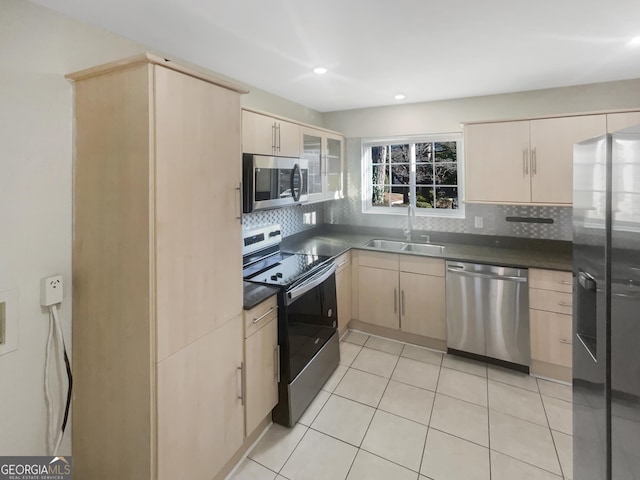 kitchen featuring a sink, appliances with stainless steel finishes, backsplash, light brown cabinetry, and dark countertops