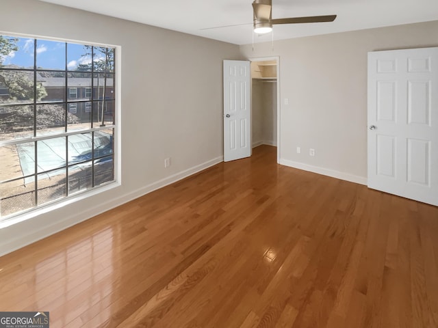 unfurnished bedroom featuring ceiling fan, a spacious closet, baseboards, and wood finished floors