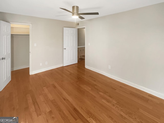 unfurnished bedroom with ceiling fan, wood finished floors, baseboards, a closet, and a walk in closet