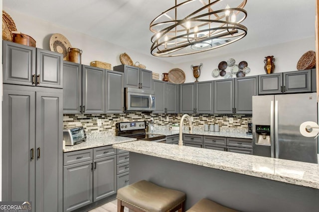 kitchen featuring a breakfast bar area, appliances with stainless steel finishes, gray cabinets, and backsplash