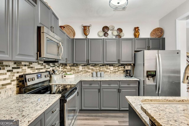 kitchen featuring appliances with stainless steel finishes, gray cabinets, light wood-style flooring, and tasteful backsplash