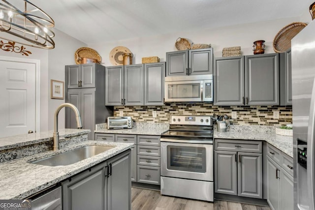 kitchen with appliances with stainless steel finishes, gray cabinets, a sink, and tasteful backsplash