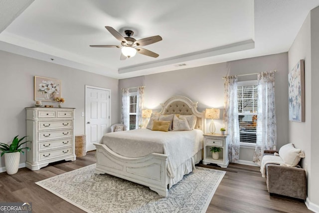 bedroom featuring baseboards, visible vents, a tray ceiling, and dark wood-style flooring