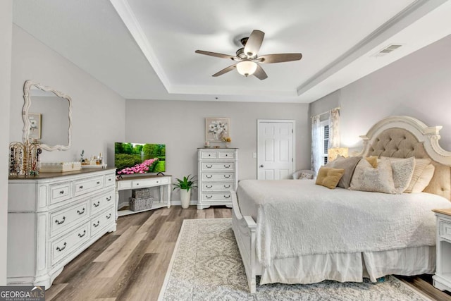 bedroom with visible vents, baseboards, a ceiling fan, wood finished floors, and a tray ceiling