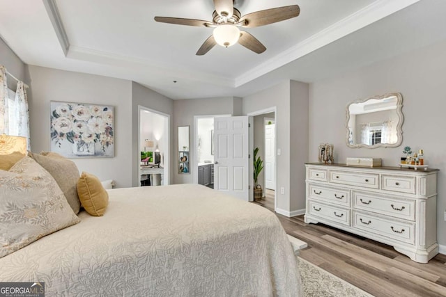 bedroom featuring baseboards, ensuite bath, ceiling fan, wood finished floors, and a tray ceiling