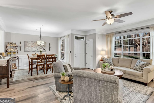 living room featuring ornamental molding, wainscoting, ceiling fan, and light wood finished floors