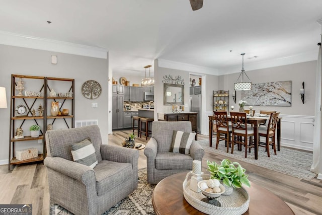 living area featuring visible vents, ornamental molding, light wood-style flooring, and a decorative wall