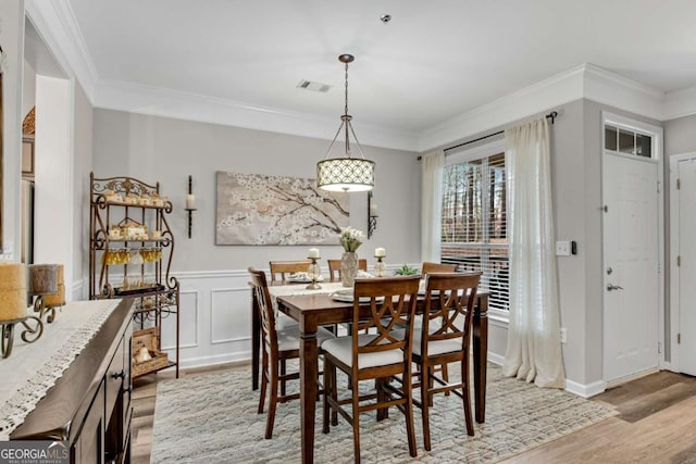 dining space with a wainscoted wall, crown molding, visible vents, and light wood finished floors