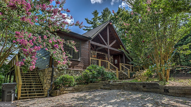 view of front of property featuring stone siding, covered porch, and stairs