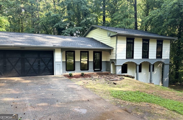 tri-level home featuring driveway, a garage, roof with shingles, brick siding, and a porch