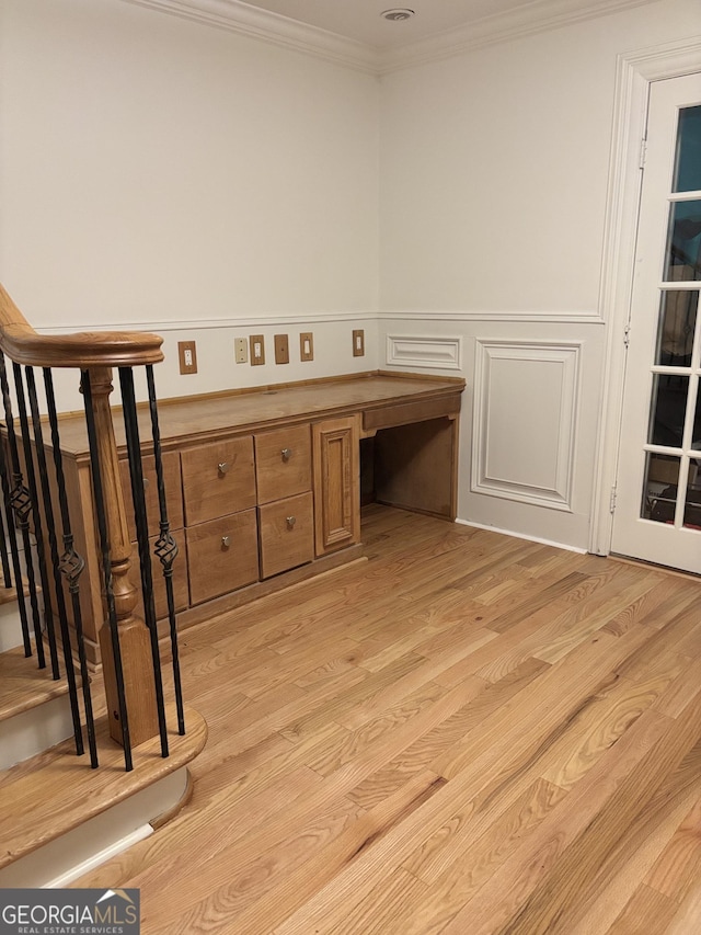 unfurnished office with ornamental molding, light wood-type flooring, built in desk, and wainscoting