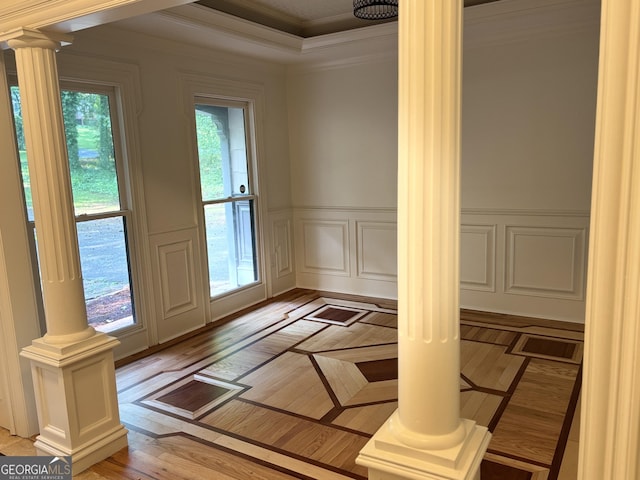 doorway with decorative columns, crown molding, wainscoting, a decorative wall, and light wood-type flooring