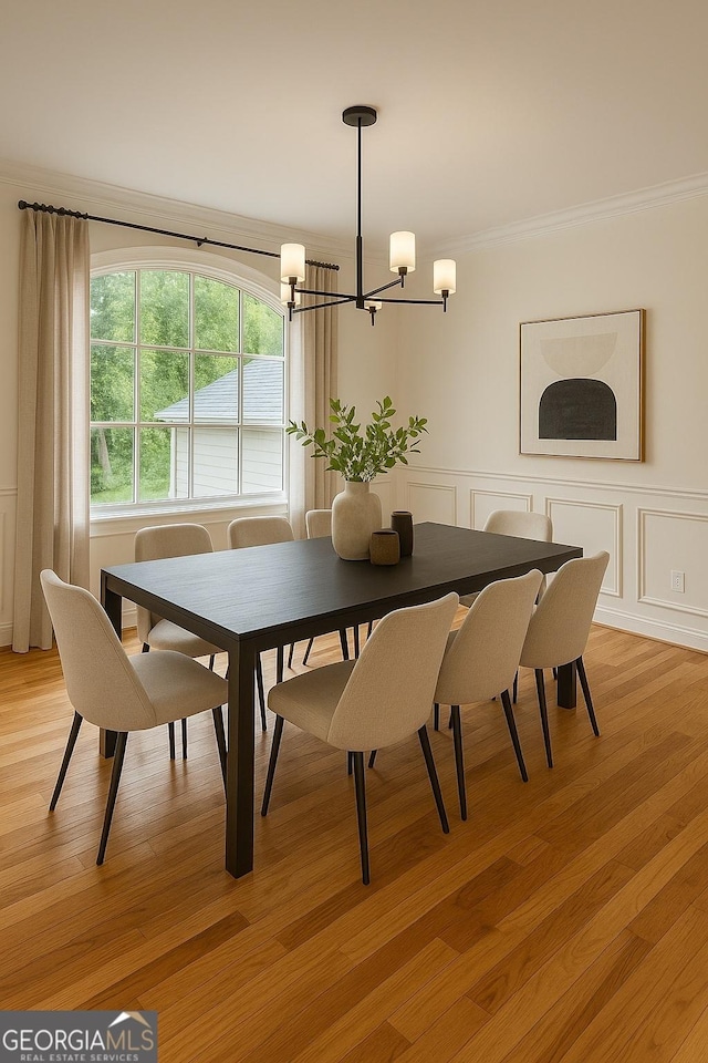 dining area featuring a chandelier, a decorative wall, crown molding, a wainscoted wall, and light wood-type flooring