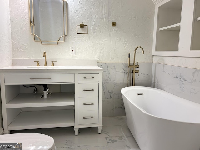 bathroom featuring a textured wall, marble look tiles, vanity, a freestanding tub, and wainscoting