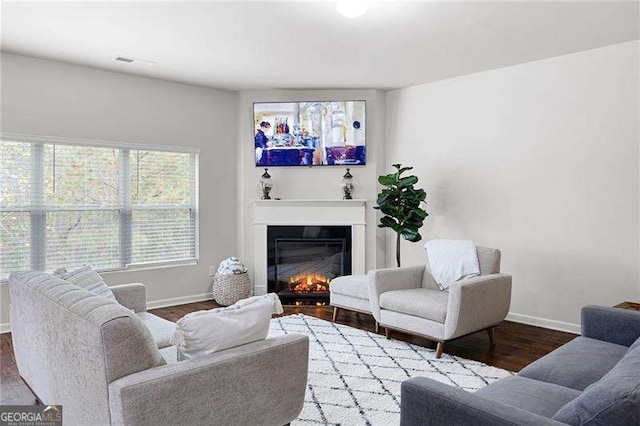 living area with a glass covered fireplace, visible vents, baseboards, and wood finished floors