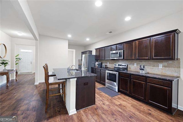 kitchen with dark wood-style floors, dark stone countertops, stainless steel appliances, and a sink