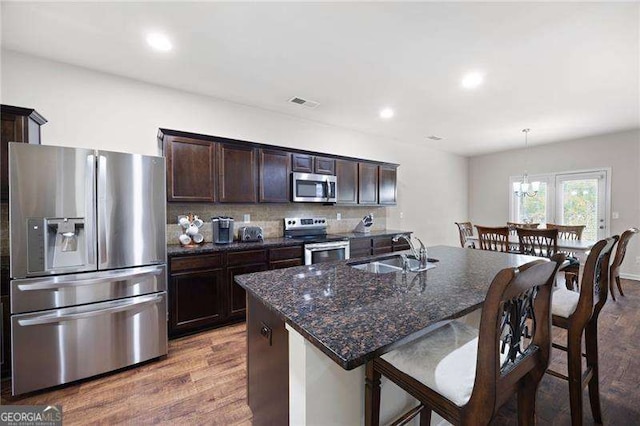 kitchen with appliances with stainless steel finishes, dark brown cabinets, a sink, and wood finished floors