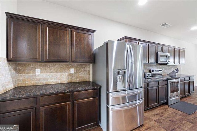 kitchen with dark brown cabinetry, dark wood-type flooring, stainless steel appliances, and backsplash