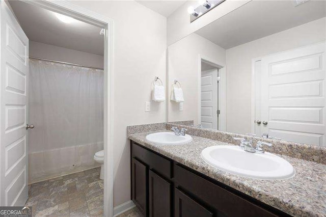 full bath featuring double vanity, stone finish floor, a sink, and toilet