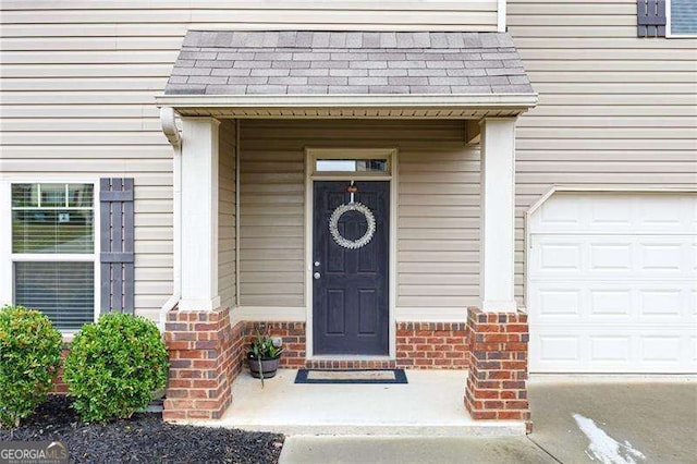 doorway to property with a garage, brick siding, and roof with shingles