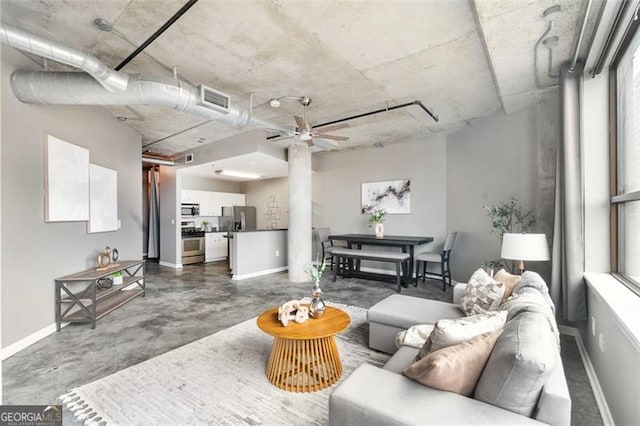 living area with finished concrete flooring, a ceiling fan, visible vents, and baseboards