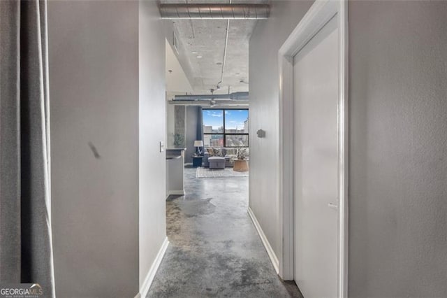 hall with attic access, concrete flooring, and baseboards