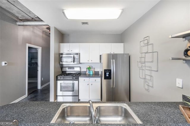 kitchen with dark countertops, stainless steel appliances, white cabinetry, open shelves, and a sink