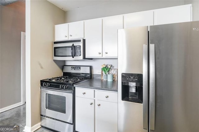 kitchen featuring stainless steel appliances, dark countertops, white cabinetry, and baseboards