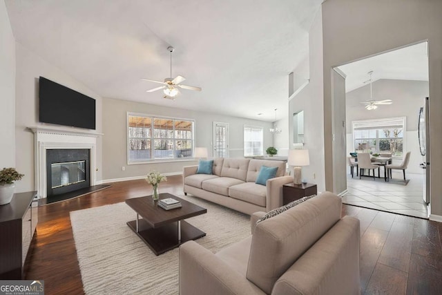 living area with ceiling fan, wood-type flooring, a glass covered fireplace, and baseboards