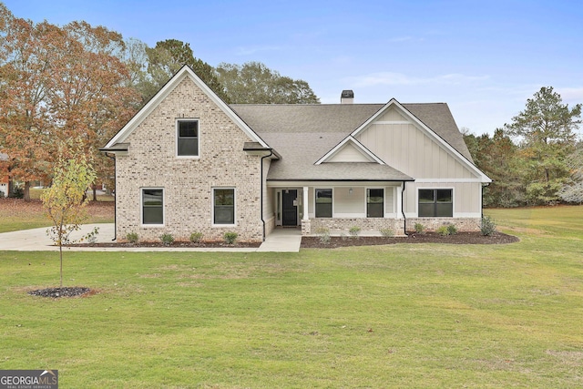 view of front of property featuring brick siding, roof with shingles, board and batten siding, a front lawn, and a chimney