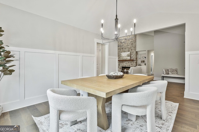 dining space with vaulted ceiling, a large fireplace, dark wood-type flooring, and a decorative wall